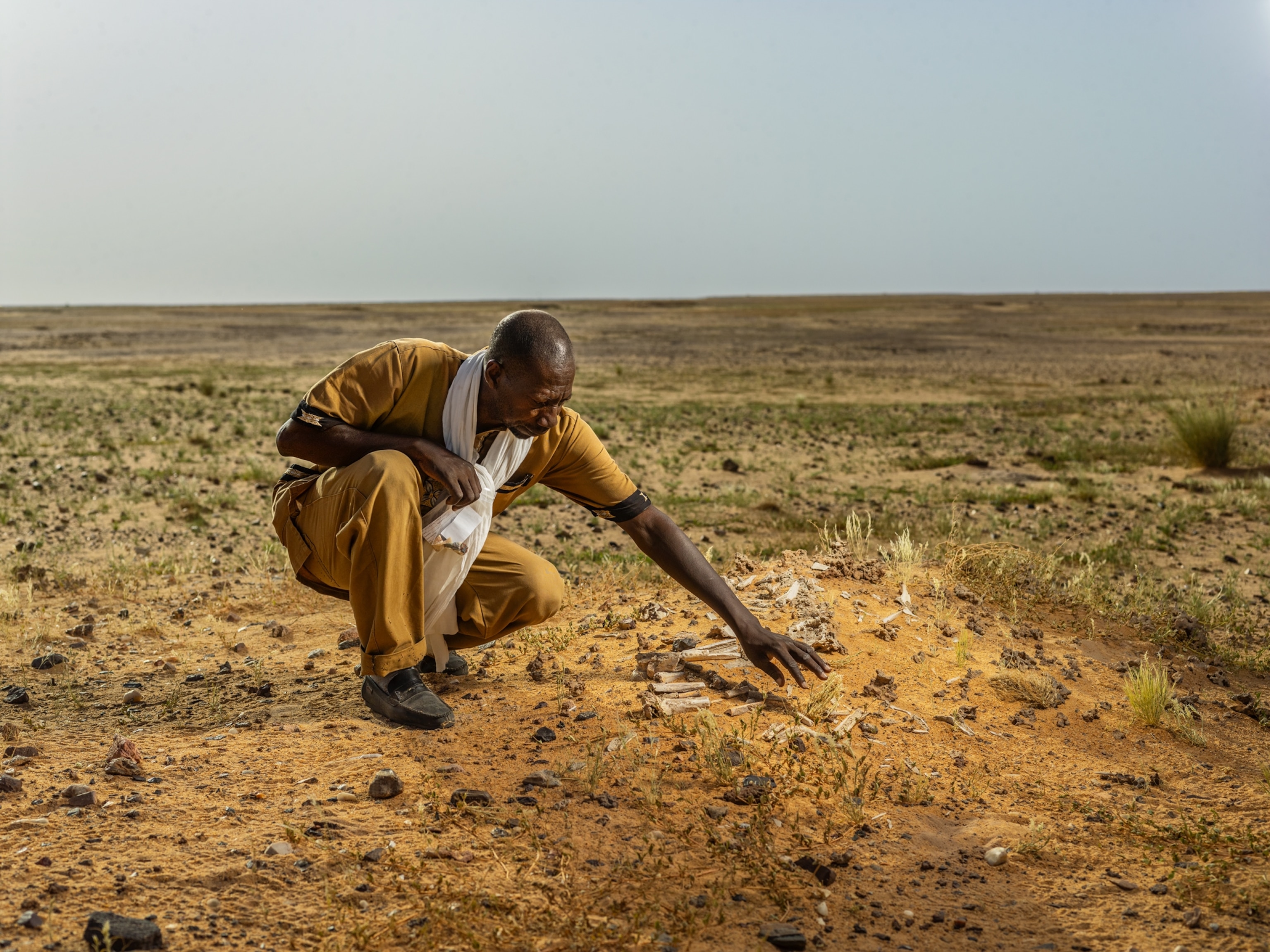 man kneeling in desert reaching out to touch broken bones on the ground