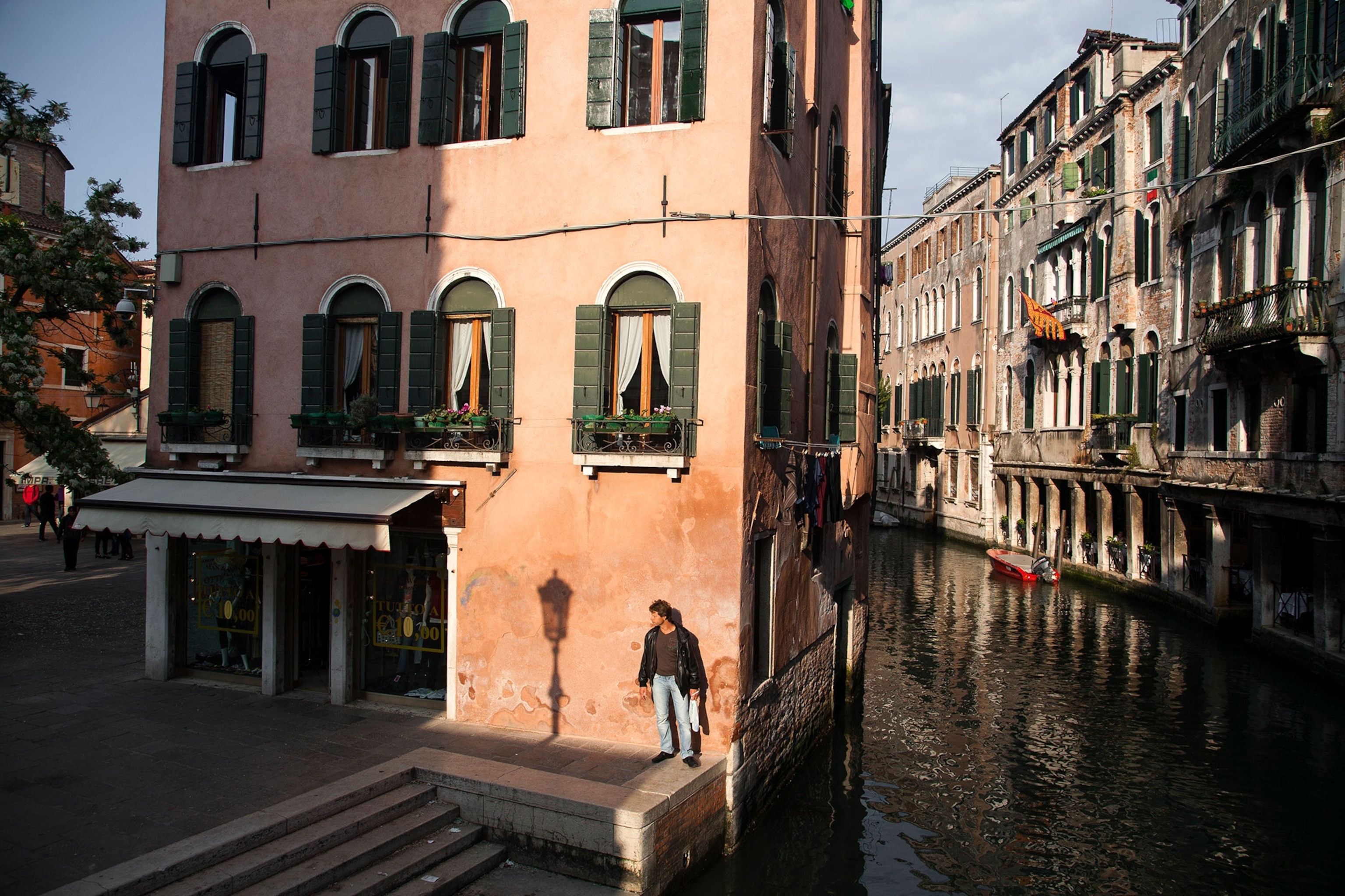 A man standing on the edge of a street by a canal with villas in Venice, Italy.